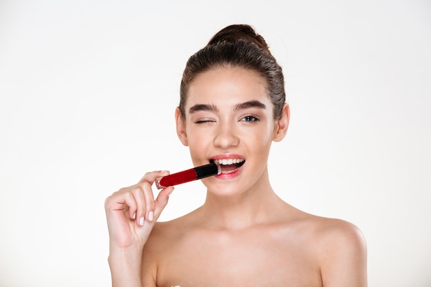 Retrato de mujer juguetona coqueteando con el pelo en moño y piel limpia con lápiz labial en la boca y guiñando un ojo