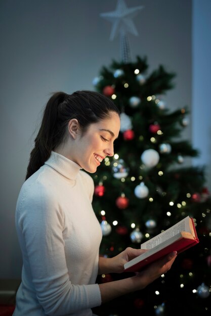 Retrato mujer leyendo junto al árbol de navidad