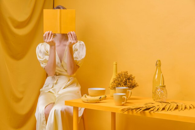 Foto gratuita retrato de mujer leyendo un libro en un escenario amarillo
