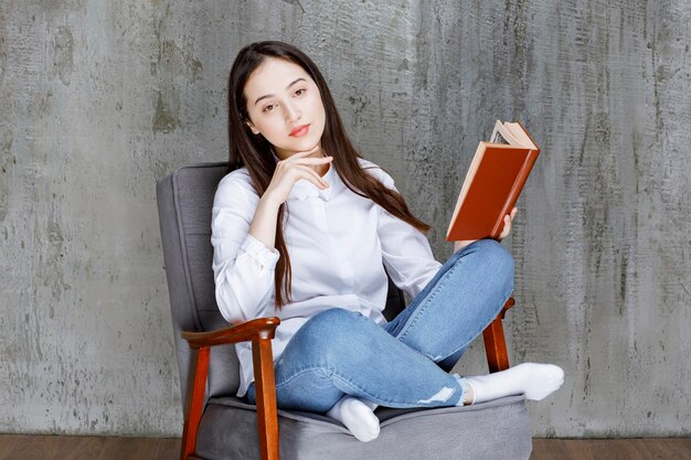 Retrato de una mujer leyendo un libro mientras se sienta en un sillón. foto de alta calidad