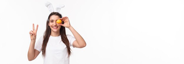 Retrato de mujer linda joven pacífica y alegre en camiseta blanca que muestra el signo de la paz y sostiene colo