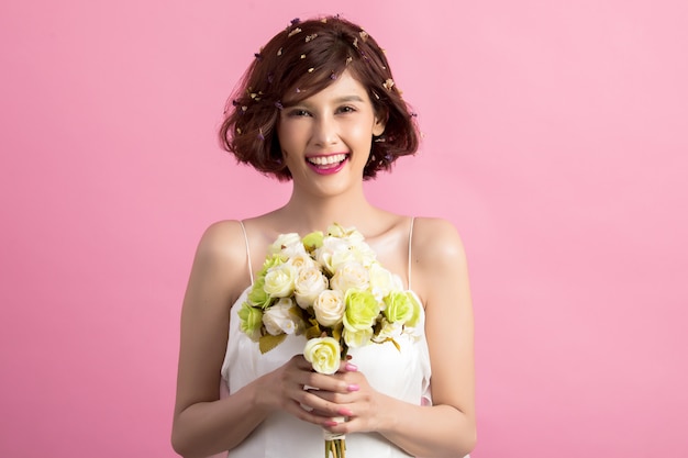 Retrato de una mujer linda juguetona sonriente que sostiene las flores aisladas en rosa