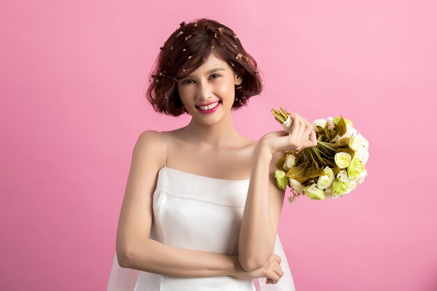 Retrato de una mujer linda juguetona sonriente que sostiene las flores aisladas en rosa