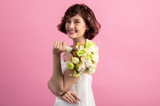 Retrato de una mujer linda juguetona sonriente que sostiene las flores aisladas en rosa