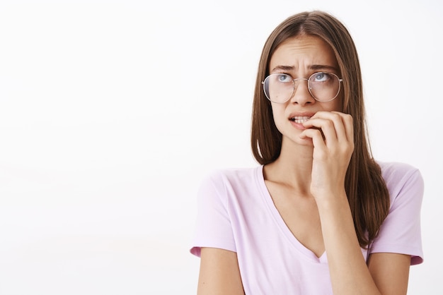 Retrato de mujer linda preocupada y preocupada en la desesperación mordiendo las uñas con el ceño fruncido mirando en la esquina superior izquierda con problemas con gafas