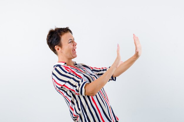 Retrato de mujer madura mostrando gesto de parada en camisa a rayas y mirando asustado vista frontal