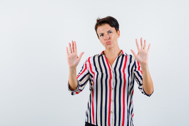 Retrato de mujer madura mostrando gesto de parada en camisa a rayas y mirando resuelto vista frontal