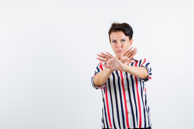 Retrato de mujer madura mostrando gesto de parada en camisa a rayas y mirando resuelto vista frontal