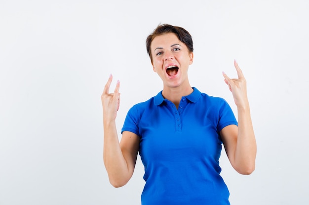 Retrato de mujer madura mostrando gesto de rock en camiseta azul y mirando enérgico vista frontal