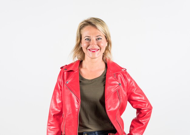 Retrato de una mujer madura rubia de moda sonriente en la chaqueta roja aislada en el contexto blanco