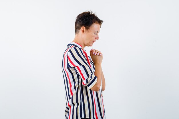 Retrato de mujer madura uniendo las manos en gesto de oración en camisa a rayas y mirando esperanzado