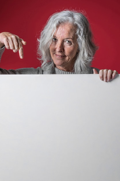 Retrato de una mujer mayor apuntando con su dedo hacia abajo el cartel blanco en blanco
