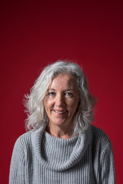 Retrato de una mujer mayor con el pelo gris corto contra el fondo rojo