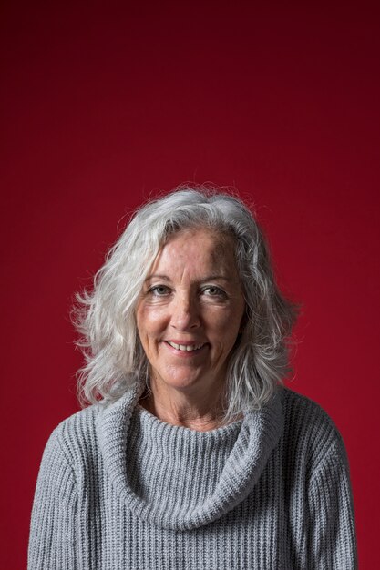 Retrato de una mujer mayor con el pelo gris corto contra el fondo rojo