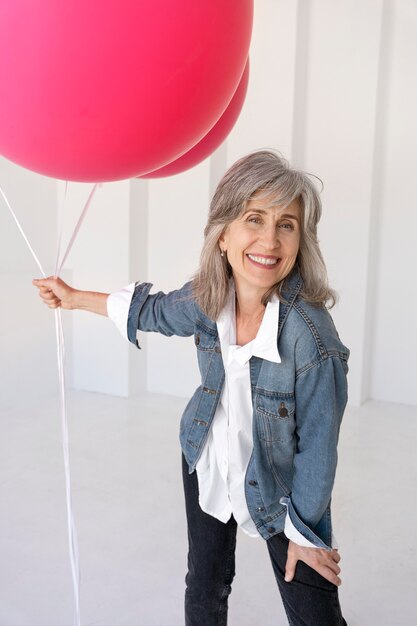 Retrato, de, mujer mayor, posar, en, un, chaqueta de jean, y, tenencia, globos rosados