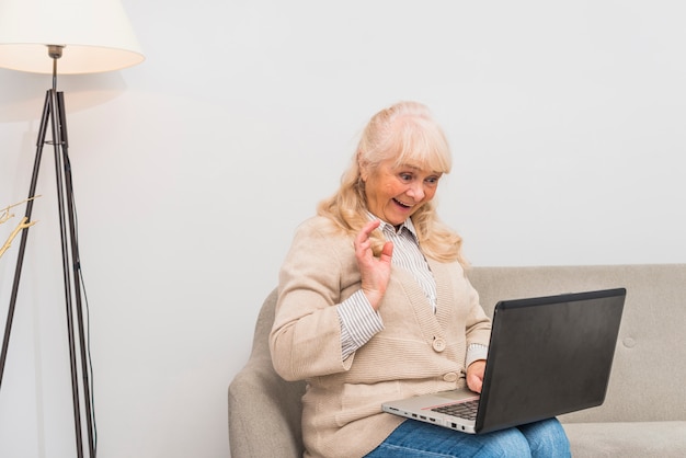 Foto gratuita retrato de una mujer mayor que agita su mano mientras usa la tableta digital