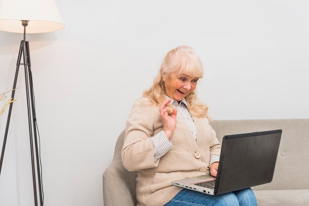 Retrato de una mujer mayor que agita su mano mientras usa la tableta digital