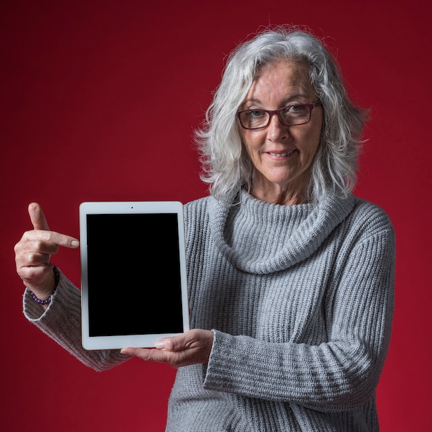 Retrato de una mujer mayor que señala su dedo en la tableta digital contra fondo coloreado