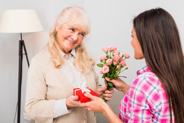 Retrato de una mujer mayor sonriente que da el regalo y las rosas a su hija joven