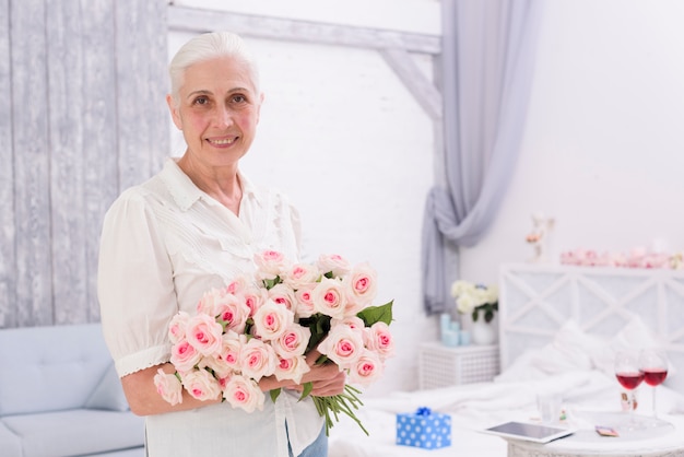 Retrato de una mujer mayor sonriente que sostiene el ramo de flores color de rosa en casa