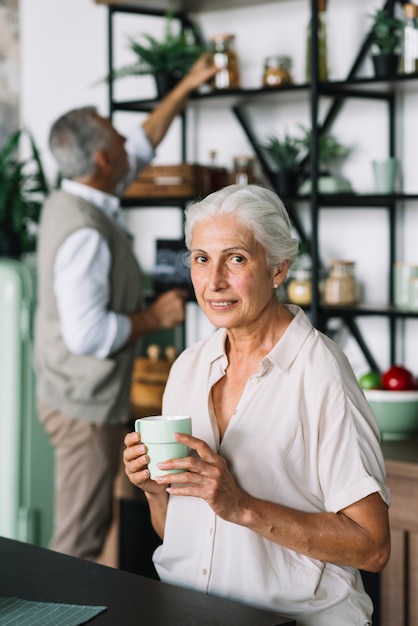 Retrato de la mujer mayor sonriente que sostiene la taza de café