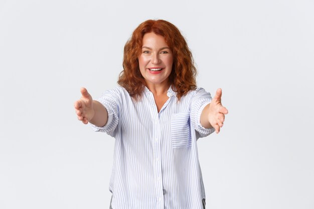 Retrato de mujer de mediana edad pelirroja feliz y encantadora extiende las manos, estirando los brazos para abrazar, madre que quiere abrazar o abrazar a alguien. Las mujeres reciben el regalo y lo toman, fondo blanco.