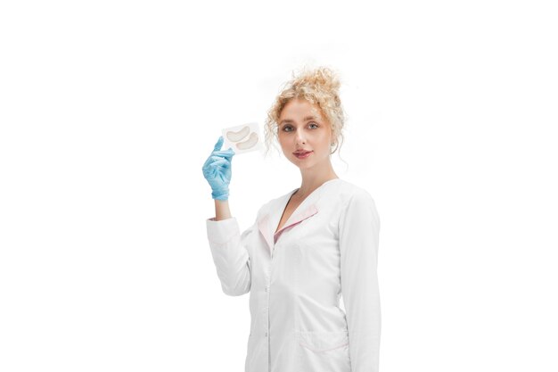 Retrato de mujer médico, enfermera o cosmetóloga en uniforme blanco y guantes azules sobre blanco.