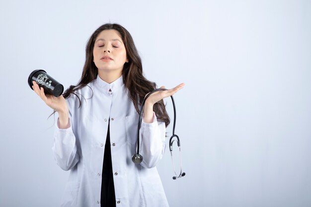 Retrato de mujer médico con estetoscopio y taza de café durmiendo en la pared blanca.