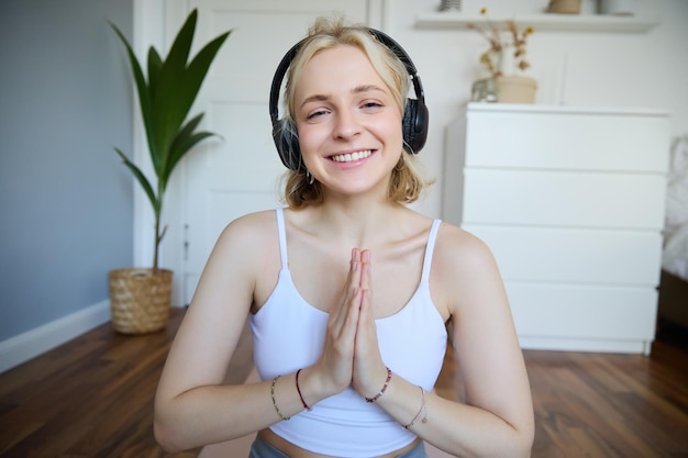 Retrato de una mujer meditando en casa sentada con auriculares escuchando un podcast de yoga tomados de la mano