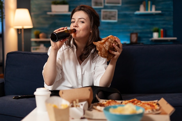 Retrato de mujer mirando a la cámara durante el almuerzo de comida rápida orden de comida relajándose en el sofá
