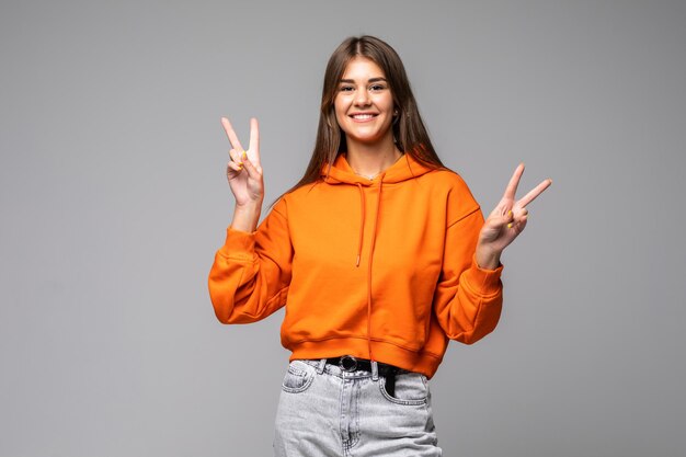 Retrato de mujer de moda alegre mostrando dos dedos firman en gris