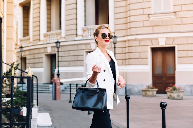 Retrato de mujer de moda en gafas de sol caminando en la calle. Ella está sonriendo a un lado.