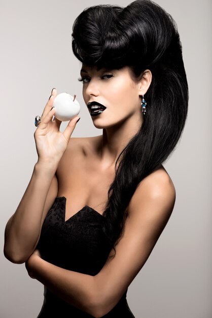 Retrato de mujer de moda con peinado moderno y labios en color negro con manzana blanca