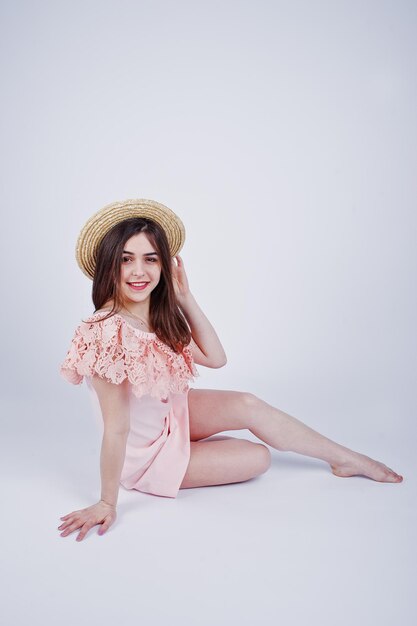 Retrato de una mujer de moda con vestido rosa sentada y posando con un sombrero en el suelo del estudio