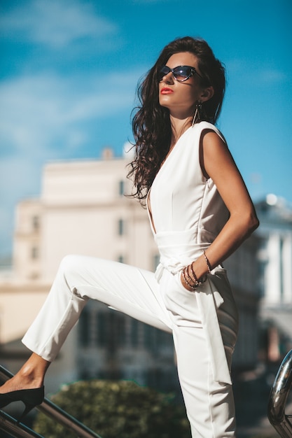 Retrato de mujer modelo. Chica caliente en traje blanco posando en la calle. Mujer de moda en gafas de sol