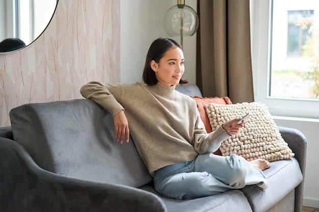 Retrato de una mujer moderna sentada en casa con un control remoto relajándose los fines de semana viendo televisión y