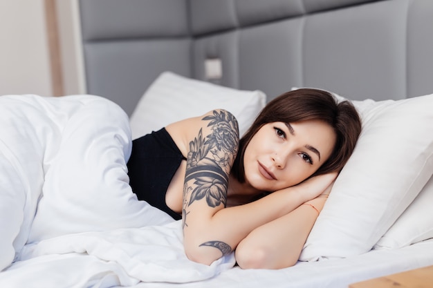 Retrato de mujer morena acostada en la cama por la mañana despierta estirando sus brazos y cuerpo