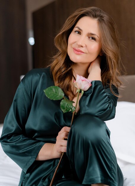 Retrato de mujer morena caucásica de pelo rizado sensual sosteniendo una flor en la mano posando sola Hermosa dama con estado de ánimo romántico pasando vacaciones en la habitación del hotel Ropa de dormir elegante Apariencia de belleza