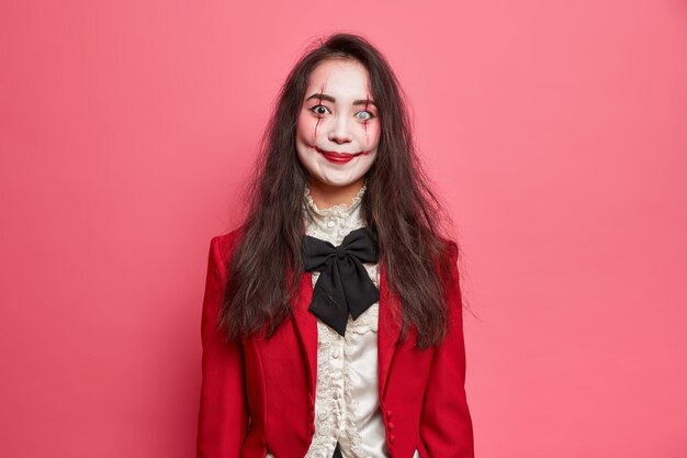 Retrato de mujer morena espeluznante viste maquillaje gótico de halloween tiene una imagen de vampiro aterrador que va a la fiesta con poses de aspecto horrible contra la pared rosada