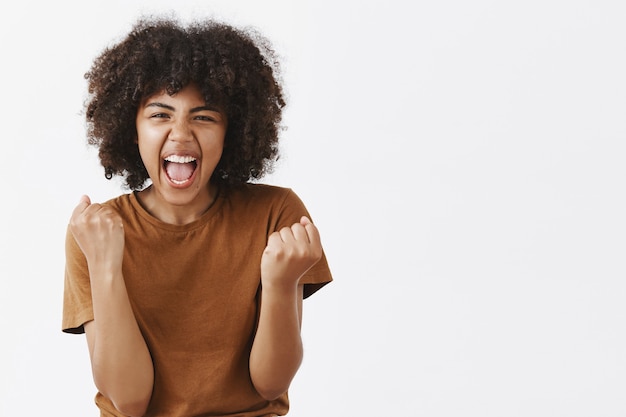 Retrato de mujer morena feliz emocionada y emotiva alegre animando al equipo favorito gritando de emoción y alegría apretando los puños en gesto de victoria o triunfo