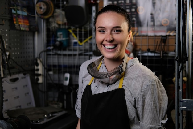 Foto gratuita retrato de una mujer morena hermosa feliz con ropa de trabajo y delantal, de pie en un taller.