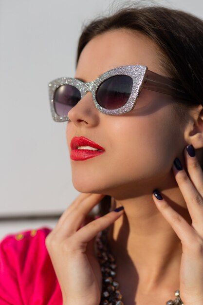 Retrato de mujer morena de moda en elegantes gafas de sol y camiseta rosa de cerca.