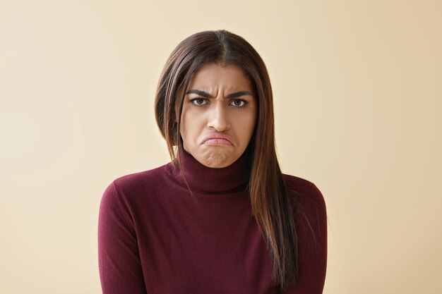 Retrato de mujer morena de raza mixta joven gruñón molesto con expresión enojada, haciendo muecas debido a un día de mala suerte o un fracaso en el trabajo. Frunciendo el ceño a una niña africana que se siente enojada, ofendida y decepcionada