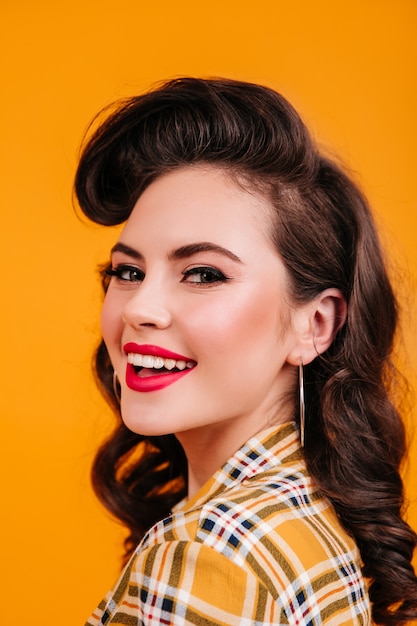 Retrato de mujer morena rizada con sonrisa encantadora. Disparo de estudio de dichosa chica pinup riendo sobre fondo amarillo.