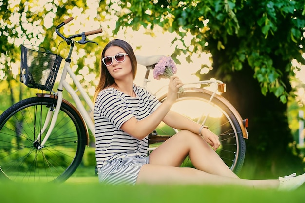 Retrato de mujer morena se sienta en un césped en un parque soleado.