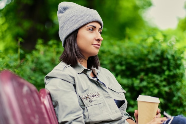 Retrato de mujer morena en un sombrero bebe café en un parque de verano.