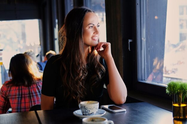 Retrato de mujer morena sonriente bebe café por la mañana en un café.