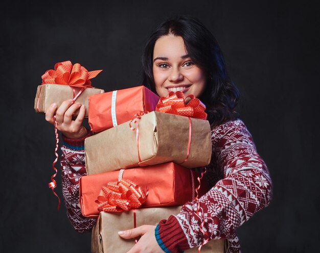 Retrato de mujer morena sonriente festiva con el pelo largo y rizado, vestida con un suéter rojo tiene regalos de Navidad.