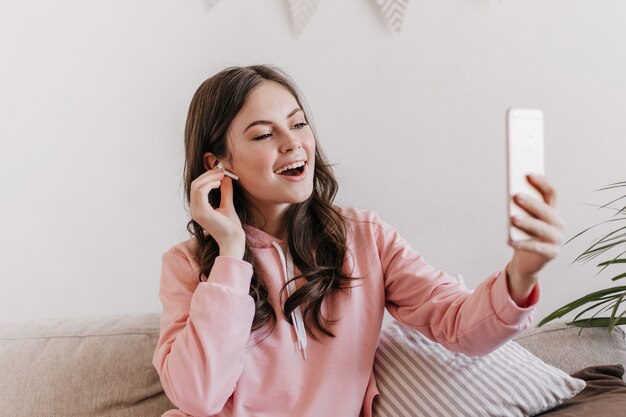 Retrato de mujer morena en sudadera con capucha rosa hablando a través de un enlace de video en el teléfono inteligente