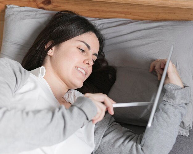 Retrato de mujer morena trabajando en tableta en la cama